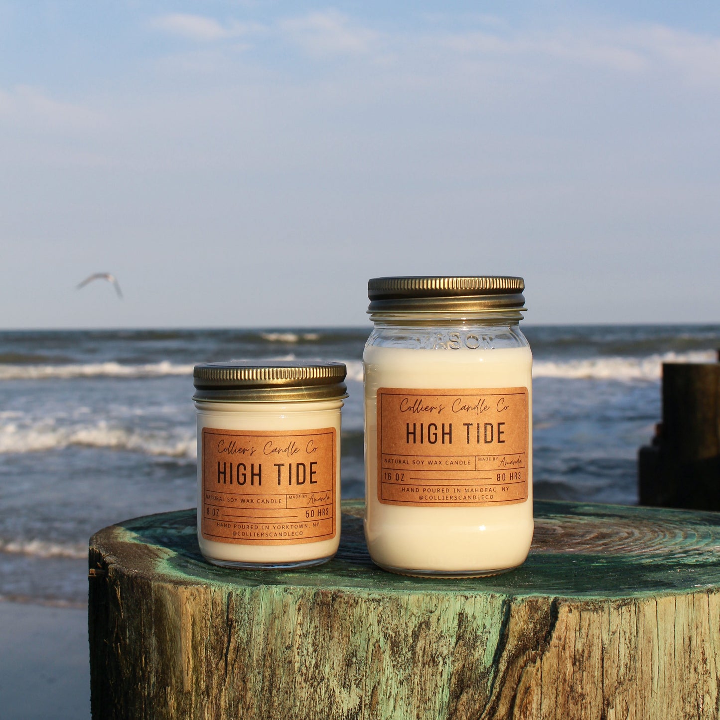 Two candles labeled 'High Tide' on a wooden post by the ocean.