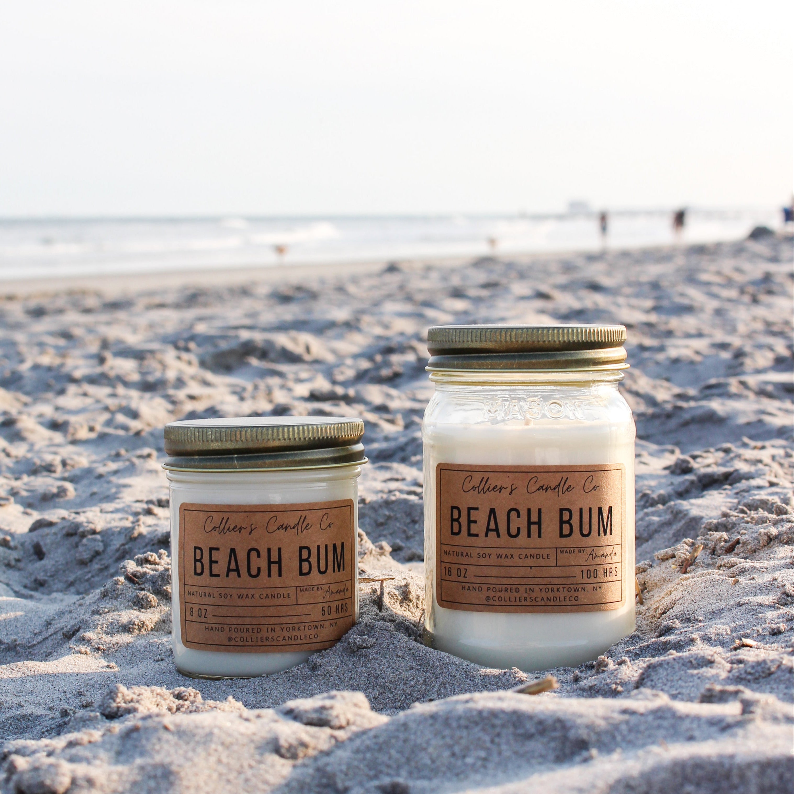 Two 'Beach Bum' candles on a sandy beach with ocean view
