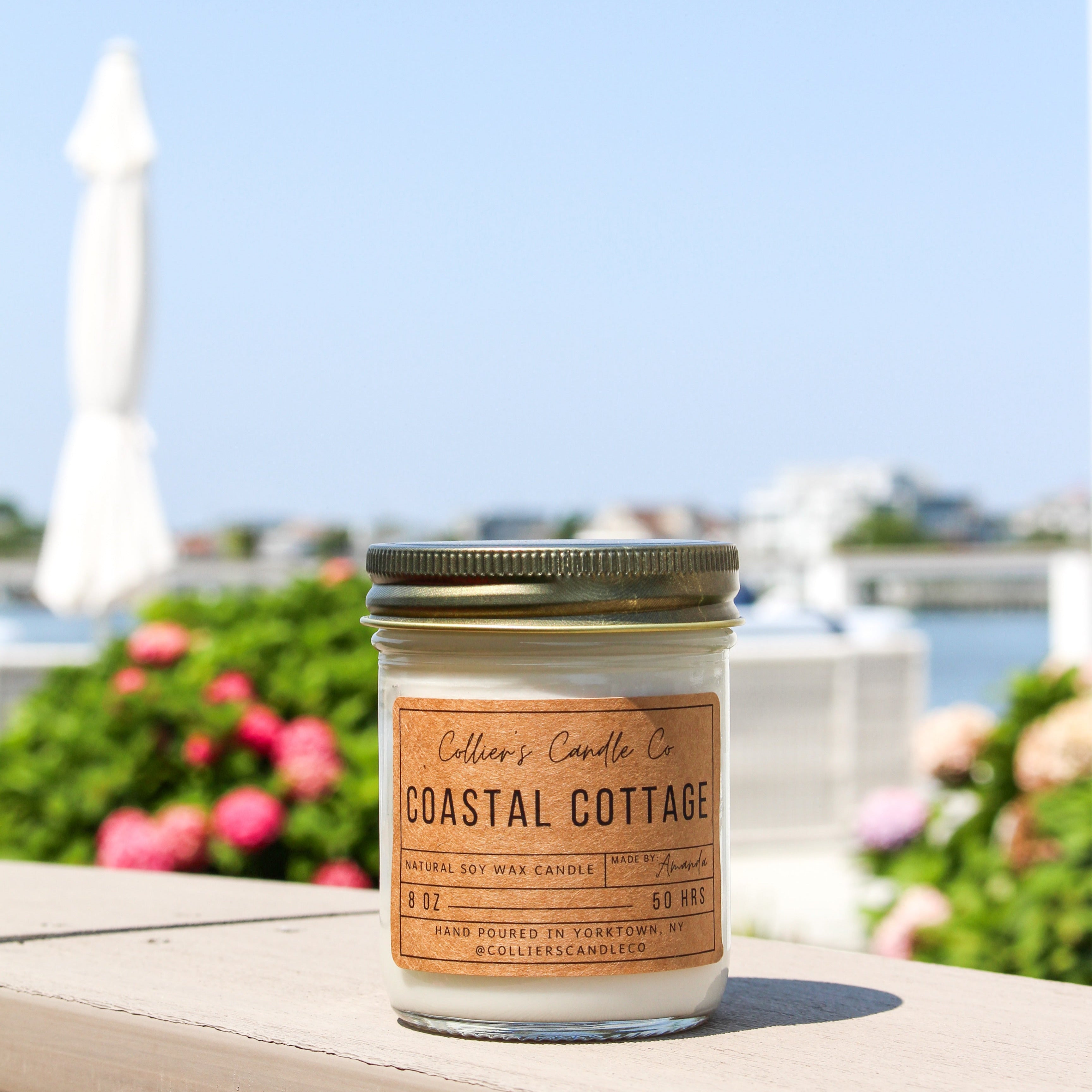 Candle labeled 'Coastal Cottage' on a ledge with a scenic background
