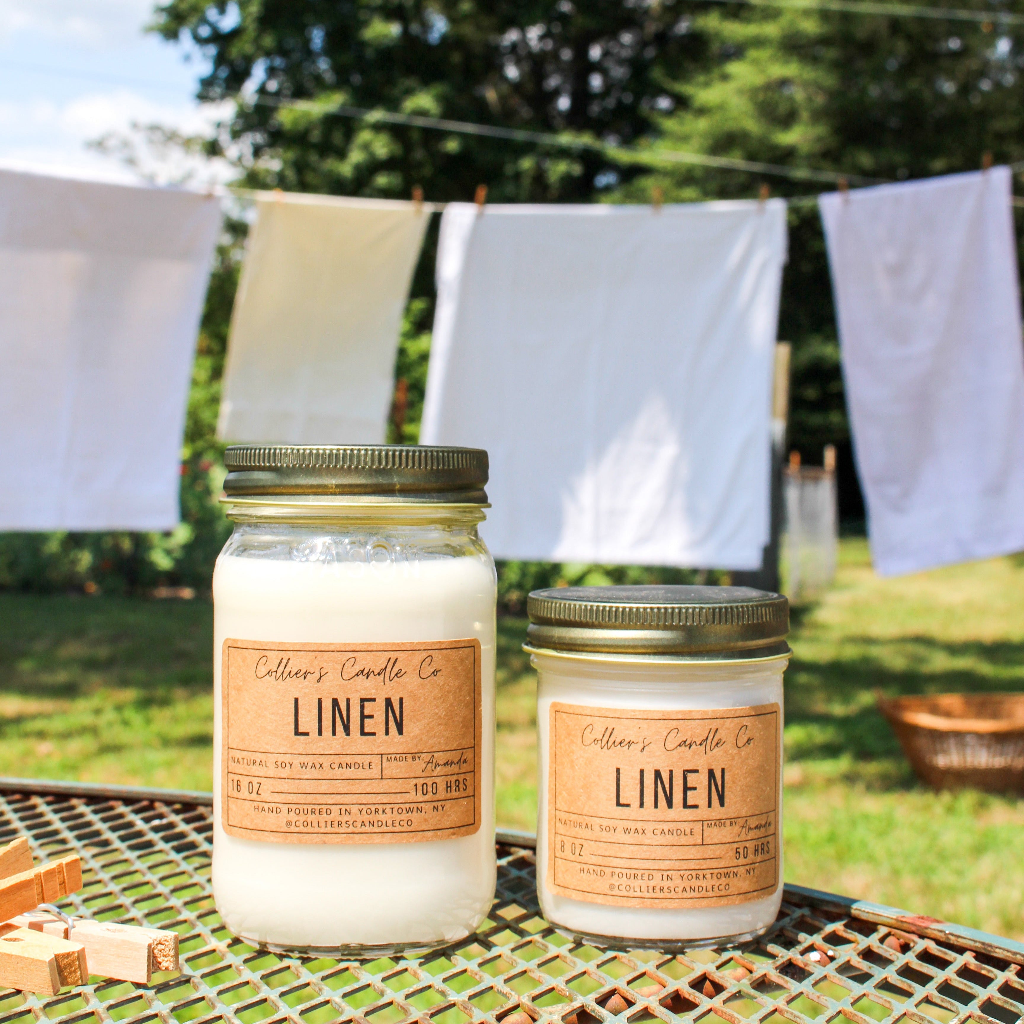 Two candles labeled 'Linen' on a table outdoors with clothesline and trees in the background