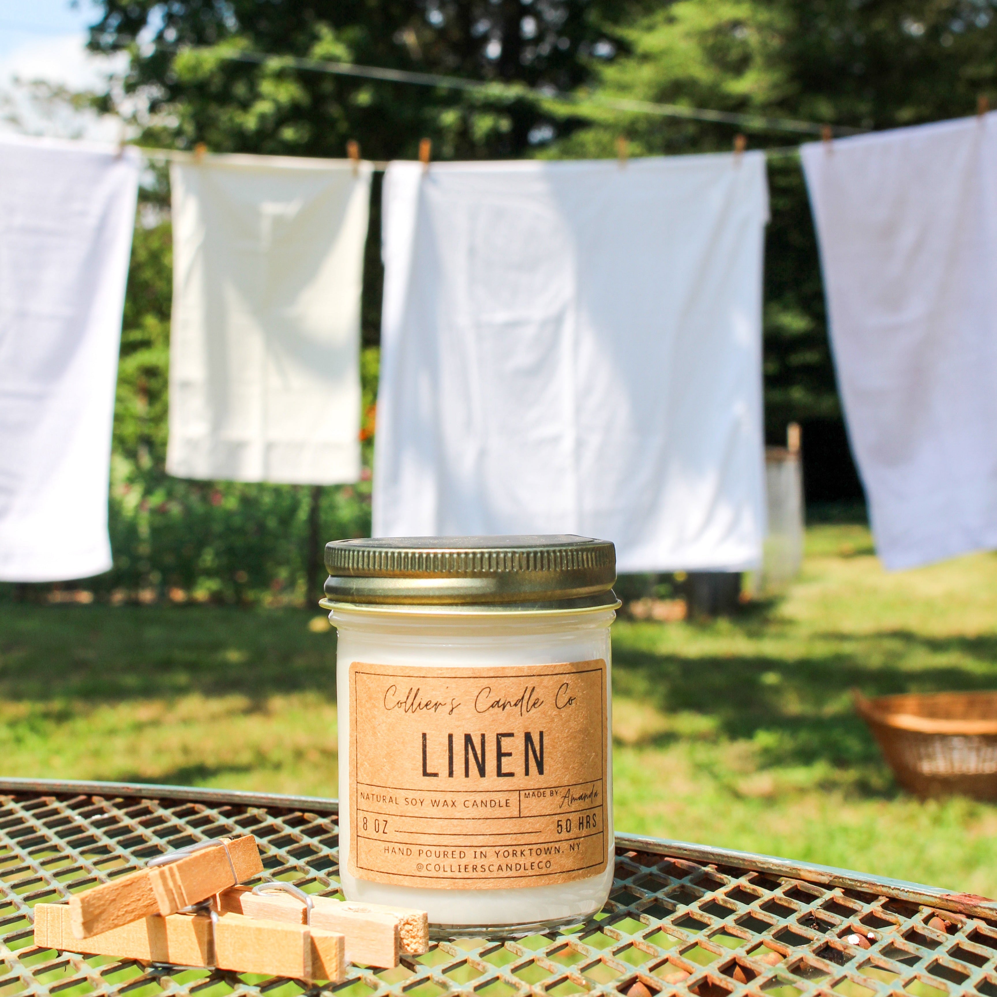 Candle labeled 'Linen' on a metal table with clothes drying in the background