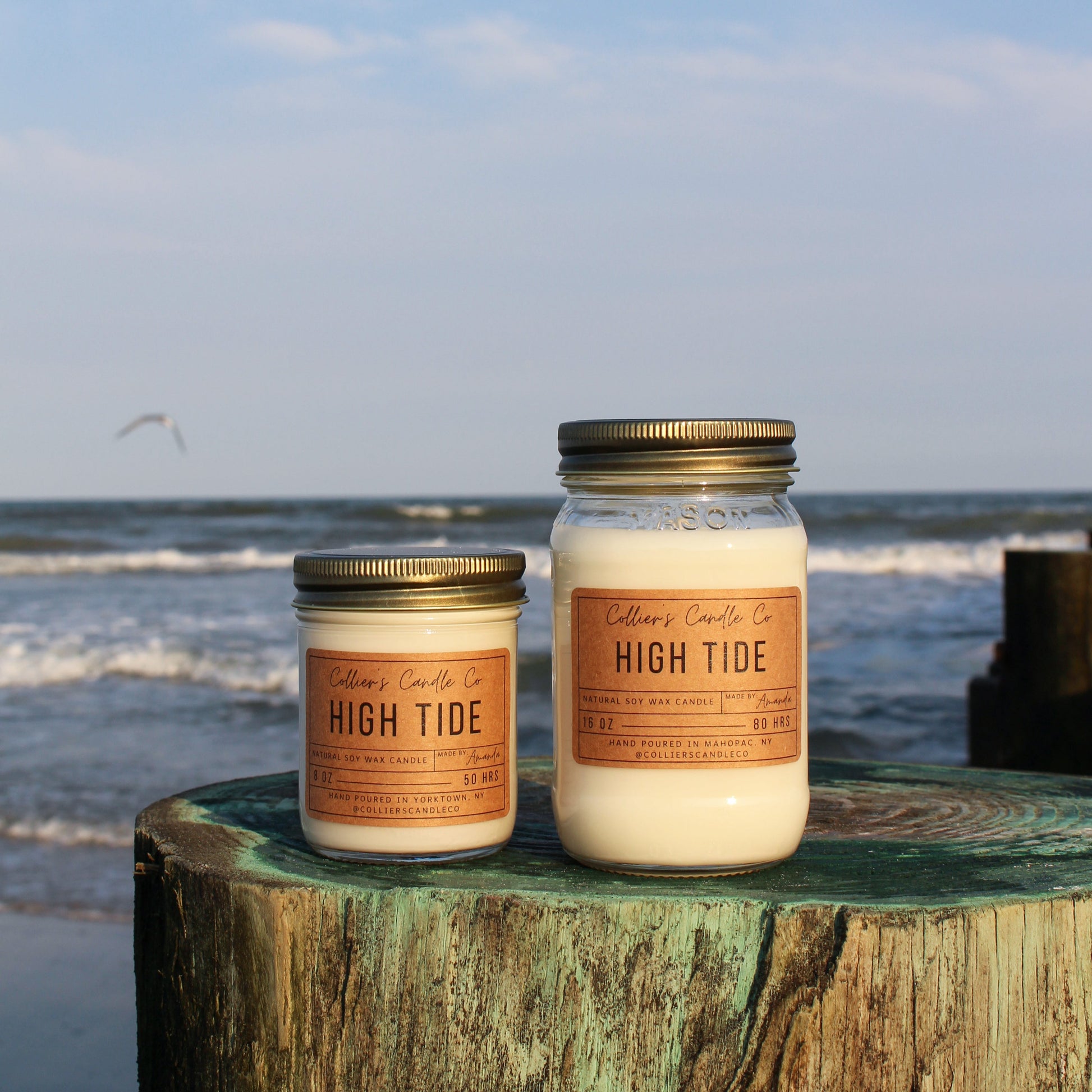 Two candles labeled 'High Tide' on a wooden post by the ocean.