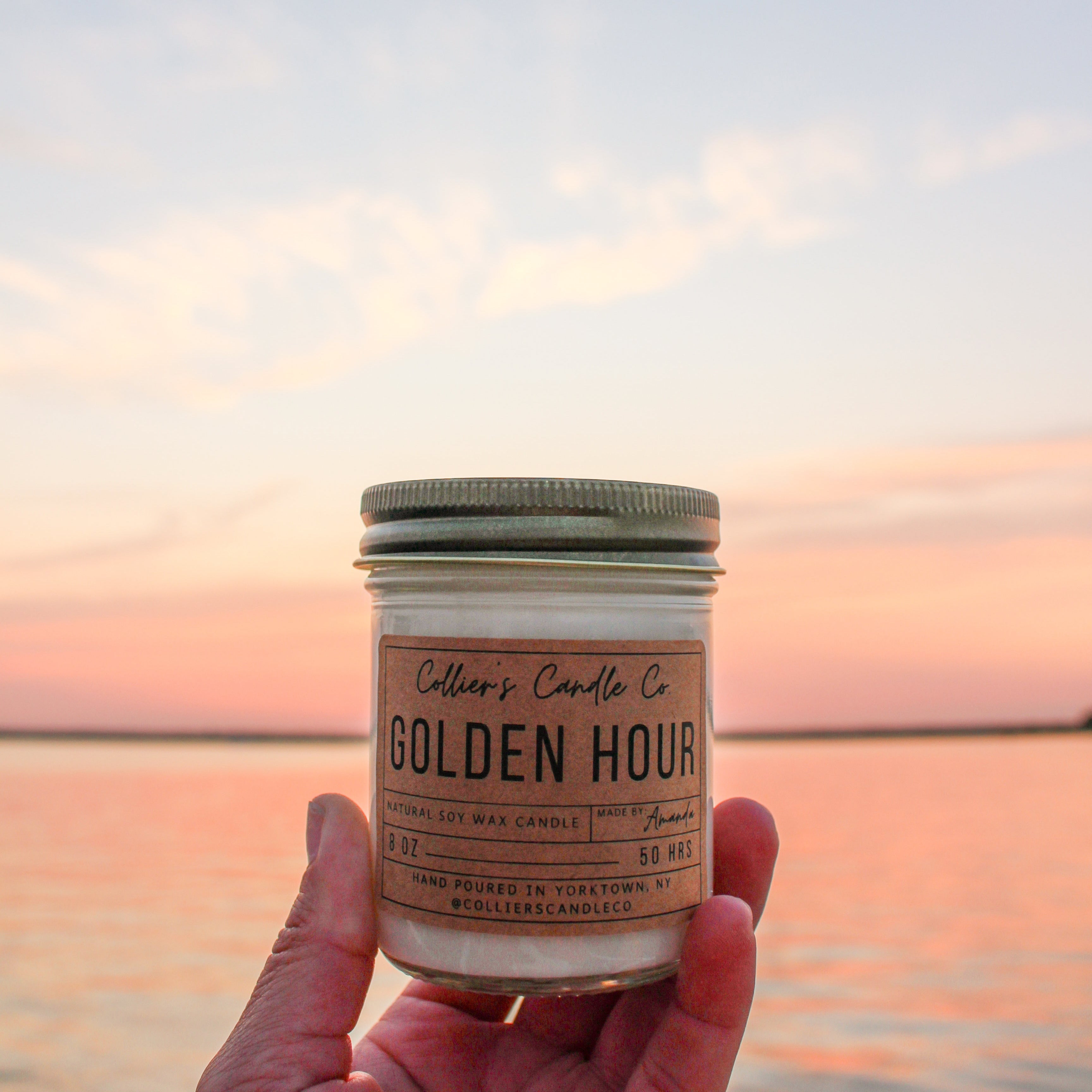 Candle labeled 'Golden Hour' held against a sunset sky.